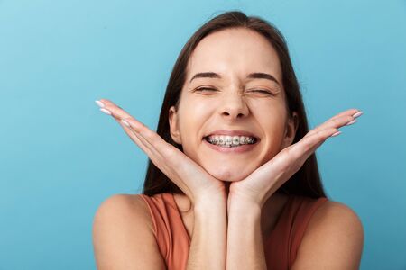 Close up of a cute lovely young girl standing isolated over blue background, grimacingの写真素材