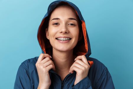 Portrait of a cheerful young girl wearing raincoat standing isolated over blue background