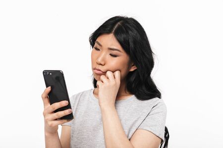 Image of asian thoughtful beautiful young woman posing isolated over white wall background using mobile phone.の写真素材