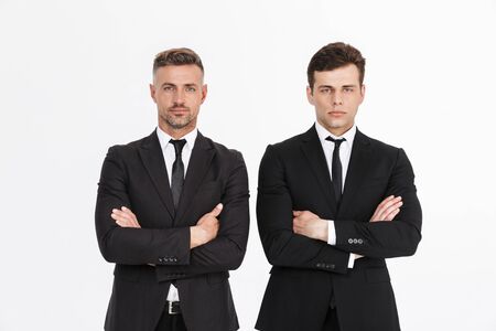Image of masculine serious two businessmen in office suits looking at camera with arms crossed isolated over gray backgroundの写真素材