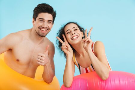 Cheerful young couple standing isolated over blue background, wearing inflatable ring