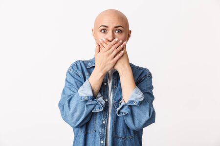 Portrait of a confused frustrated beautiful young hairless woman wearing casual clothes standing isolated over white background, cover mouthの写真素材