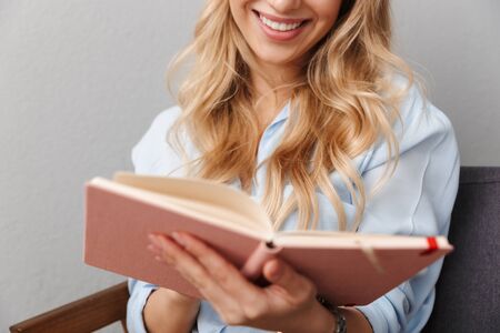 Cropped image of a happy young pretty blonde business woman posing isolated grey wall background reading book.の写真素材