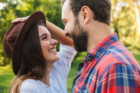 Image of joyful couple man and woman dressed in casual wear laughing while looking at each other in green parkの写真素材