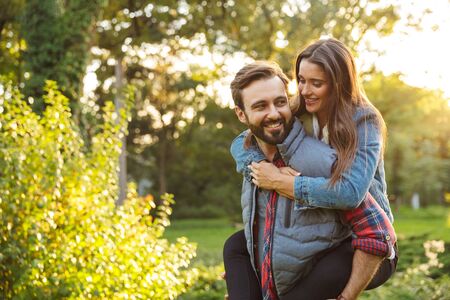Image of masculine man dressed in casual wear giving piggyback ride to nice woman in green parkの写真素材