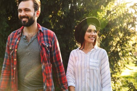 Image of young couple man and woman dressed in casual wear smiling and walking in green parkの写真素材