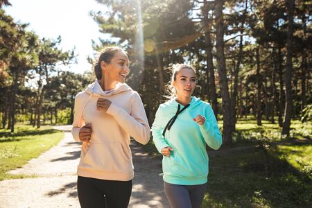 Attractive smiling fitness woman wearing hoodies working out at the park, runningの写真素材