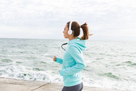 Attractive confident healthy fitness woman wearing headphones exercising outdoors at the beach,...