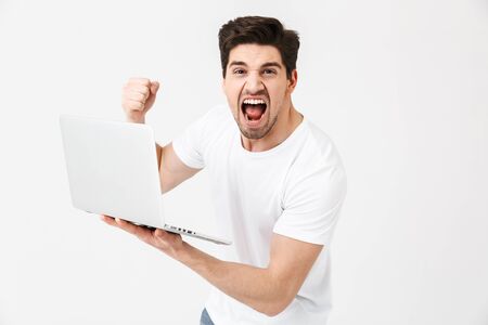Image of shocked screaming young man posing isolated over white wall using laptop computer.の写真素材