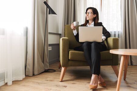 Photo of a beautiful young business woman in formal wear clothes indoors at home work with laptop computer drinking coffee.の写真素材
