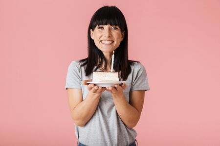 Image of a beautiful young woman posing isolated over pink wall background holding holiday birthday cake.の写真素材
