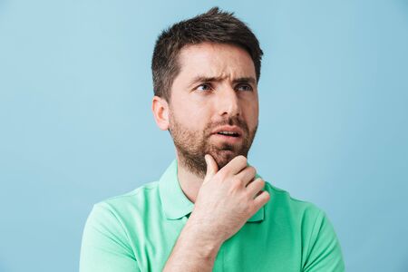 Image of a thinking serious young handsome bearded man posing isolated over blue wall background.