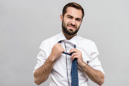 Portrait of a tired handsome young businessman wearing white shirt and tie standing isolated over gray backgroundの写真素材