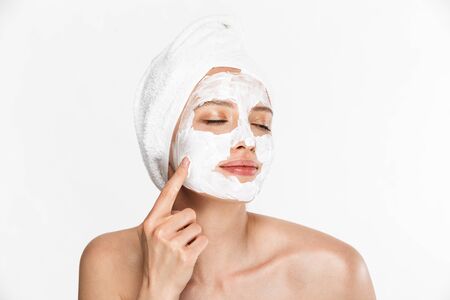 Image of pleased half-naked woman wrapped in towel applying facial cream with closed eyes isolated over white backgroundの写真素材