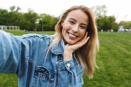 Image of amazing excited happy young woman posing outdoors in park take a selfie by camera.の写真素材