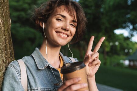 Attractive cheerful young girl wearing casual outfit spending time outdoors at the park, listening...