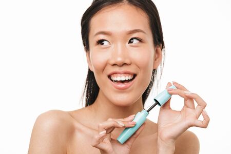 Image of a young happy cheerful beautiful asian woman posing isolated over white wall background holding makeup mascara.の写真素材