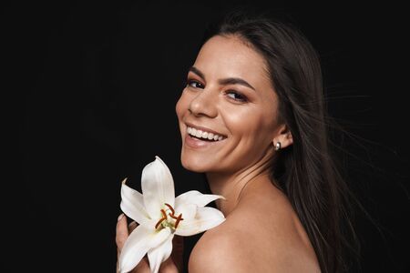Beauty portrait of an attractive young topless woman with long brunette hair isolated over black background, posing with orchid flowerの写真素材