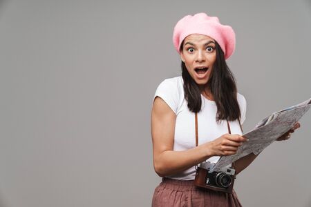Image closeup of surprised young tourist woman with retro vintage camera wondering and holding paper map isolated over gray backgroundの写真素材