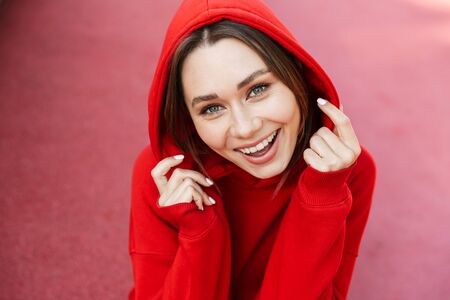 Close up of a smiling young girl wearing hoodie sitting outdoors, looking at cameraの写真素材
