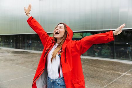 Image of beautiful excited emotional young happy pretty woman in raincoat posing outdoors.の写真素材