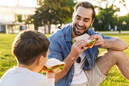 Happy young father having a picnic with his little son at the park, eating sandwichesの写真素材