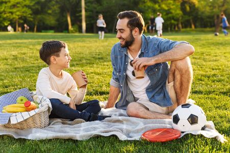 Happy young father having a picnic with his little son at the park, drinking from a cupの写真素材