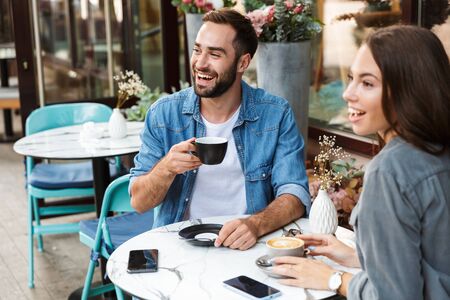 Attractive young couple in love having lunch while sitting at the cafe table outdoors, drinking coffee, talkingの写真素材