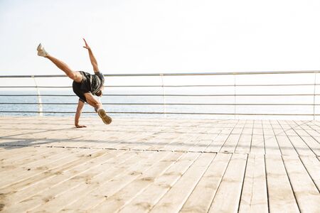 Photo of handsome strong young sports man at the beach near sea jumping make extreme exercises.