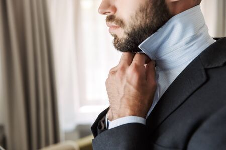 Cropped image of an attractive young businessman wearing suit standing at the hotel room, dressing...