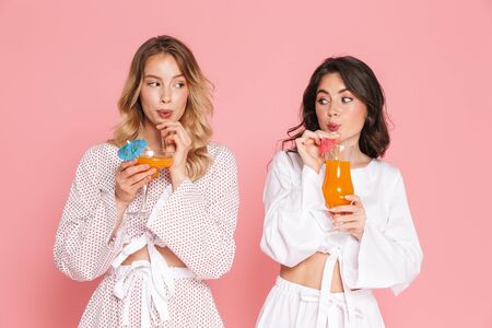 Image of excited young pretty women friends posing isolated over pink wall background drinking cocktails.の写真素材
