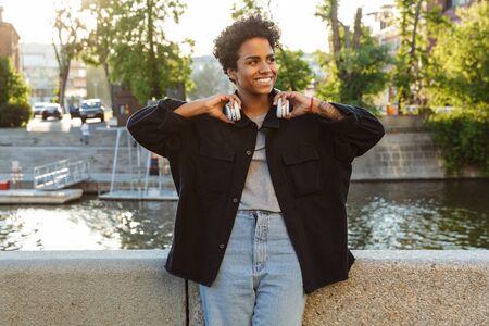 Portrait of cheerful african american woman with curly afro hairstyle holding headphones while...