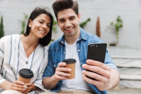 Blurred image of young couple man and woman in casual clothes drinking takeaway coffee and using...