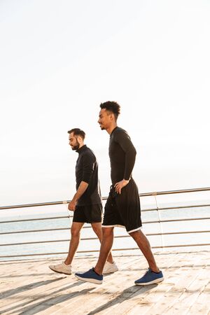 Two attractive confident young healthy sportsmen walking outdoors at the beachの写真素材