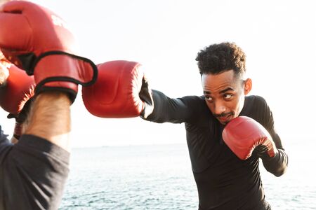 Photo of serious handsome strong two young sports men boxers friends at the beach near sea boxing.の写真素材