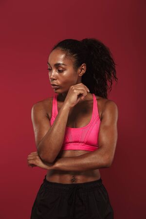Picture of a concentrated strong young african fitness sports woman posing isolated over red wall background make stretching exercises.の写真素材