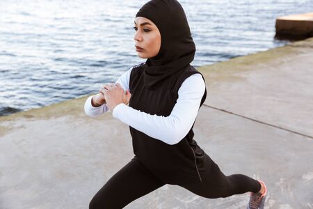 Attractive muslim sportswoman wearing hijab outdoors, doing stretching exercisesの写真素材