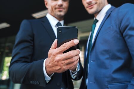 Portrait of handsome businessmen partners dressed in formal suit standing outside job center and using cellphone together during working meetingの写真素材