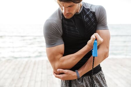 Photo of athletic man in tracksuit doing exercise with expander while working out on wooden pier at...