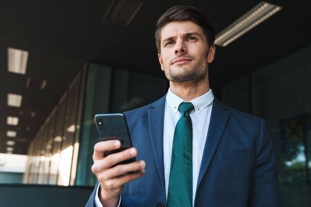 Image of a serious concentrated young business man outdoors at the street near business center using...