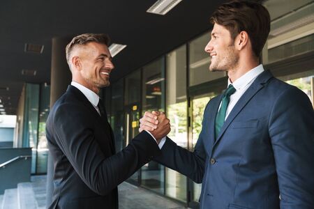Portrait closeup of two handsome businessmen partners dressed in formal suit shaking hands outside...