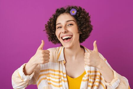 Portrait of an attractive happy young woman with curly brunette hair standing isolated over violet...