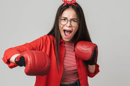 Aggressive teenage girl wearing casual outfit standing isolated over gray background, wearing boxing gloves, boxingの写真素材