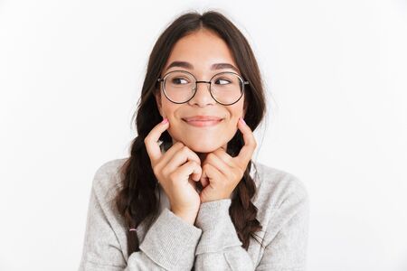 Photo closeup of caucasian teenage girl wearing eyeglasses smiling and pointing fingers at her cheeks isolated over white backgroundの写真素材