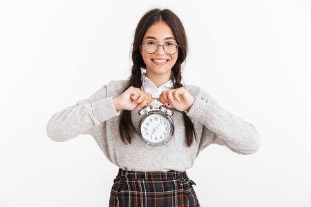 Photo closeup of pretty teenage girl wearing eyeglasses smiling while holding alarm clock in hands isolated over white backgroundの写真素材