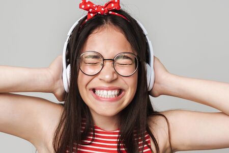 Image of excited young displeased teenage girl dressed in bright red t-shirt listening music isolated over grey wall background.の写真素材