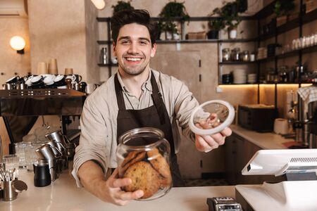 Image of handsome happy coffee man posing in cafe bar working indoors holding cookies.の写真素材