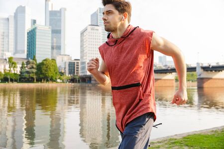 Photo of young athletic man wearing sportswear running while working out near city riverfrontの写真素材