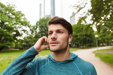 Photo closeup of handsome man wearing sportswear listening music with earphones while working out in...