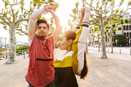 Photo of athletic concentrated man and woman wearing sportswear doing exercises while working out in city boulevardの写真素材
